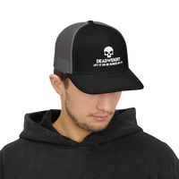 DailyThreadCo. black and grey trucker cap with skull logo worn by a man in a black hoodie.