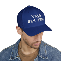 DailyThreadCo. blue structured FlexFit cap with white Bang the Iron gothic embroidery worn by a man in a denim jacket.