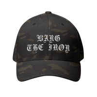 DailyThreadCo. structured FlexFit cap in dark camo with white Bang the Iron gothic embroidery on the front.