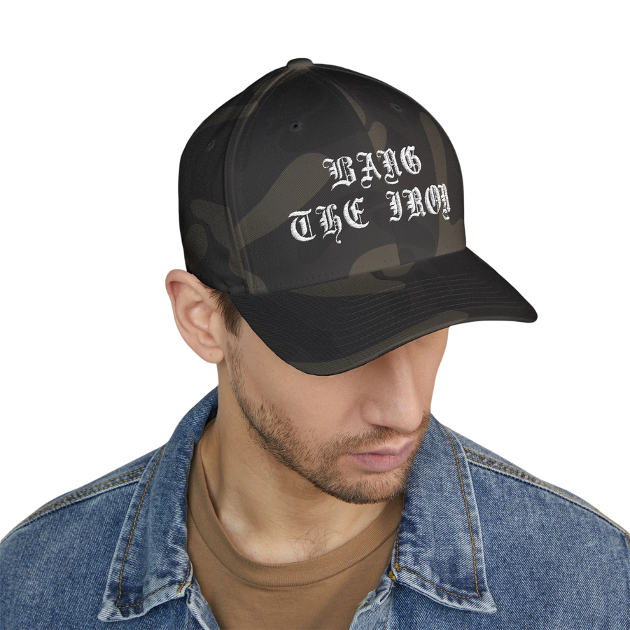 DailyThreadCo. structured FlexFit cap in camo print with white Bang the Iron gothic embroidery on the front.