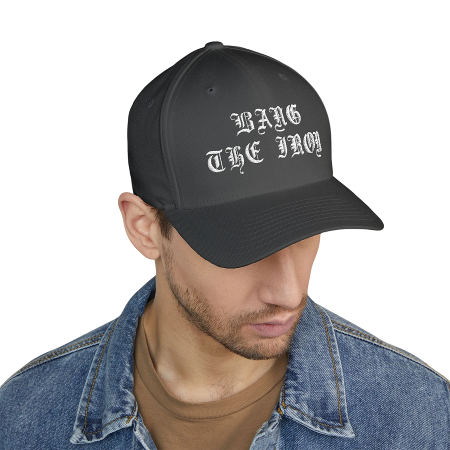 DailyThreadCo. structured FlexFit cap in dark grey with white gothic Bang the Iron embroidery on a man in denim