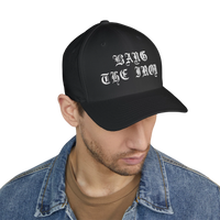 DailyThreadCo. black structured FlexFit cap with white Bang the Iron gothic embroidery worn by a man in denim jacket.