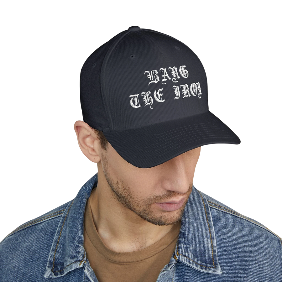 DailyThreadCo. structured FlexFit cap in black with white Bang the Iron gothic embroidery worn by a man.
