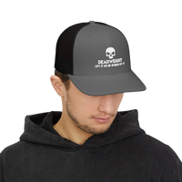 DailyThreadCo. grey and black trucker cap with a white skull Deadweight logo worn by a man in a black hoodie.